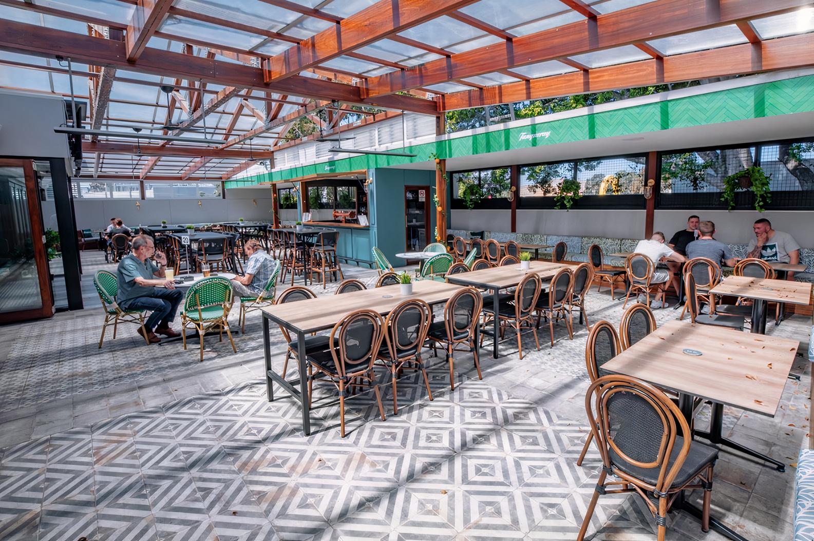 A hotel terrace with patterned tile flooring, wooden tables, rattan chairs, and a glass roof at Southern Cross Hotel.