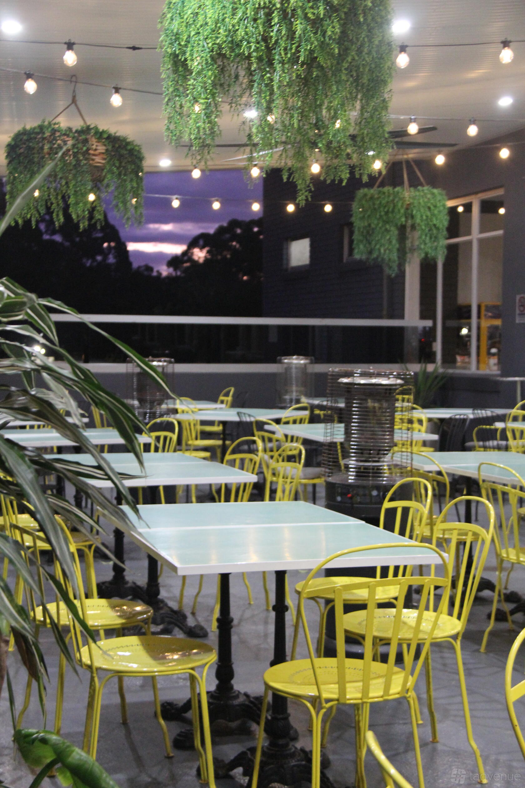 An open-air dining area with pale blue tables, yellow chairs, and outdoor heaters at Berowra RSL Club.