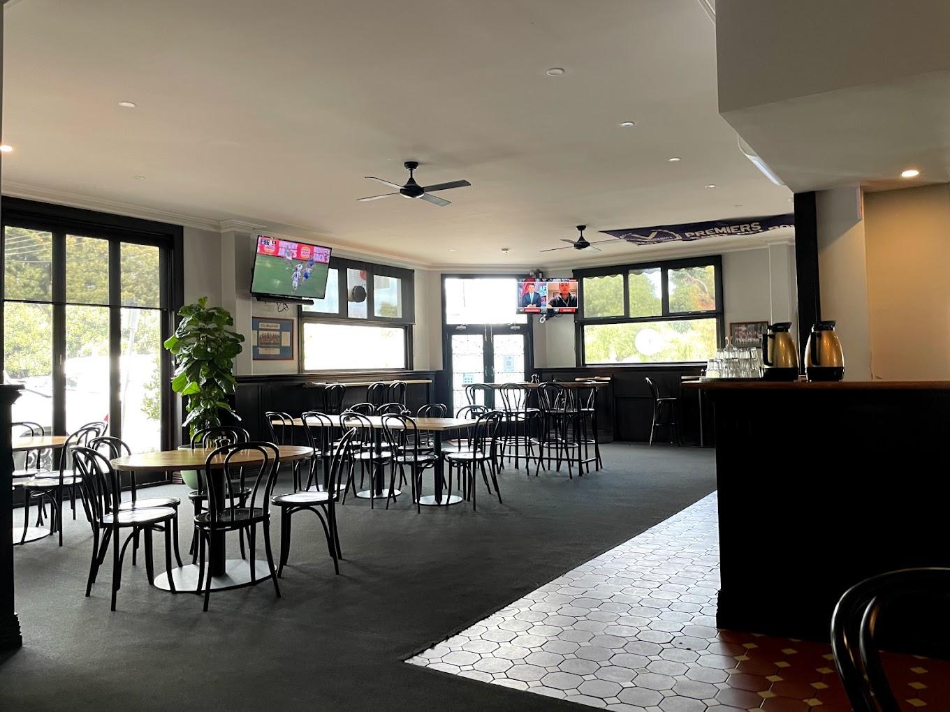 A spacious pub with large windows, multiple TVs, black bentwood chairs, and wooden tables at North Port Hotel.