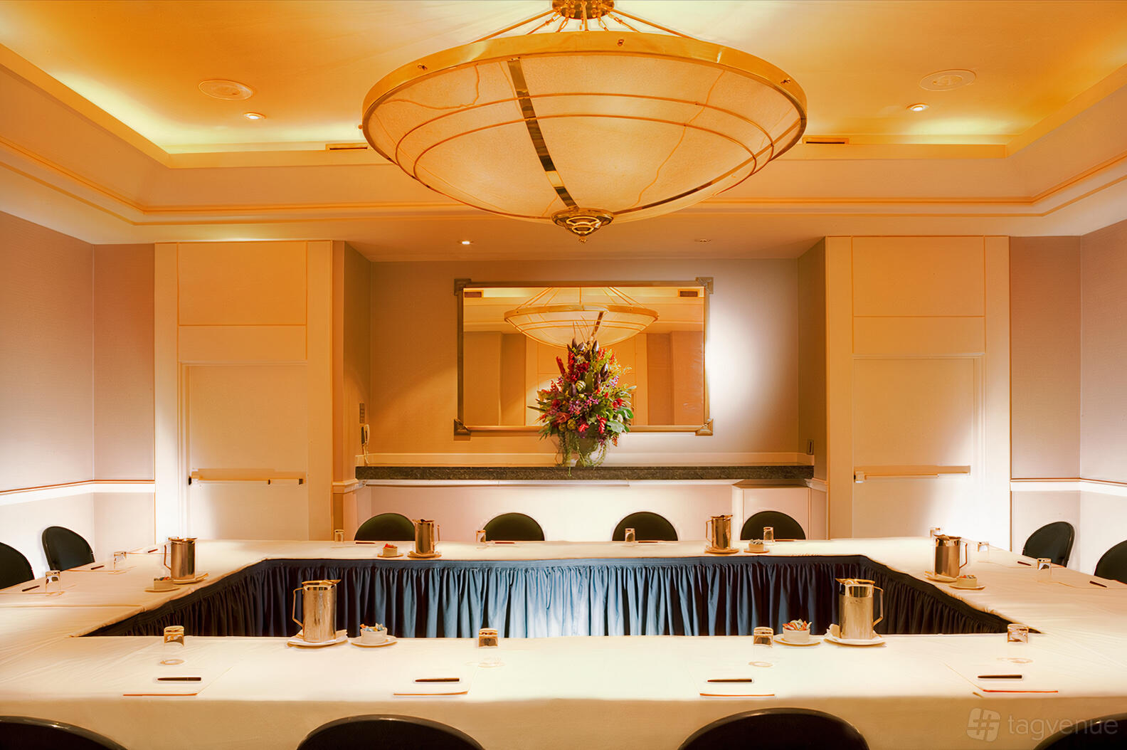 A hotel meeting room with a U-shaped table setup, upholstered chairs, and a large ceiling light at Stamford Plaza Sydney Airport Hotel.