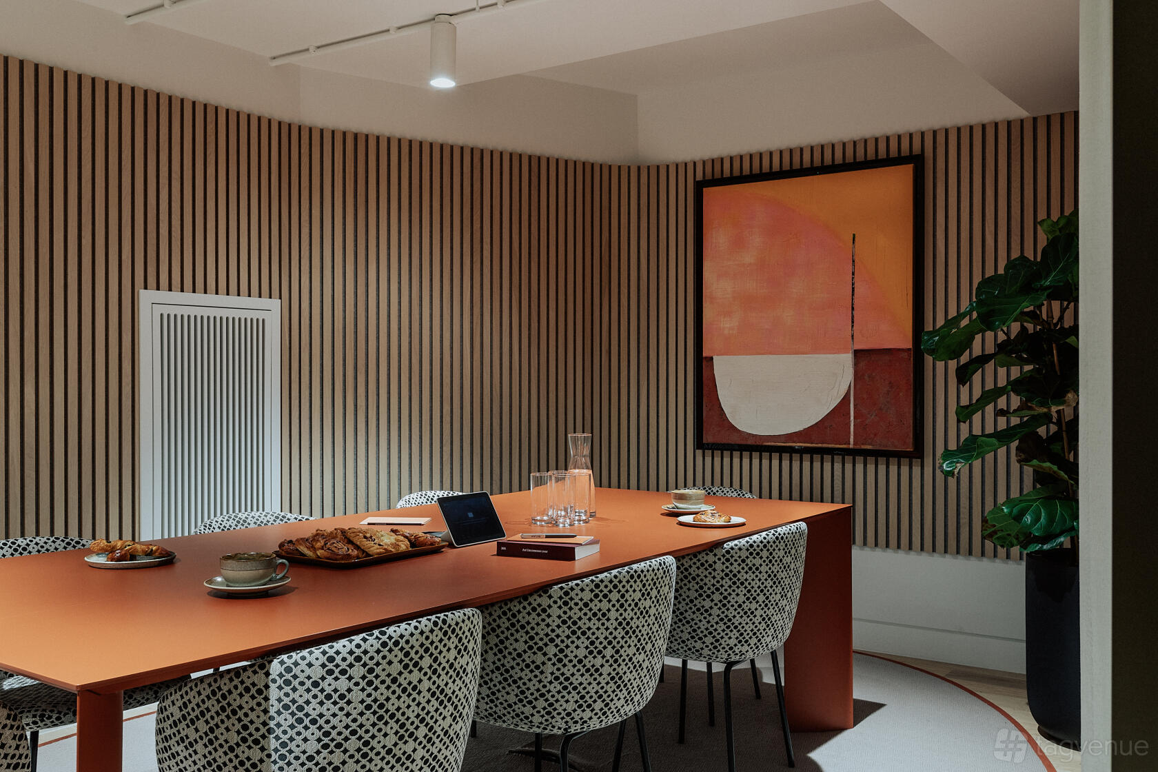 A meeting room with a long orange table, patterned chairs, wood slat walls, and abstract artwork at Uncommon Holborn.