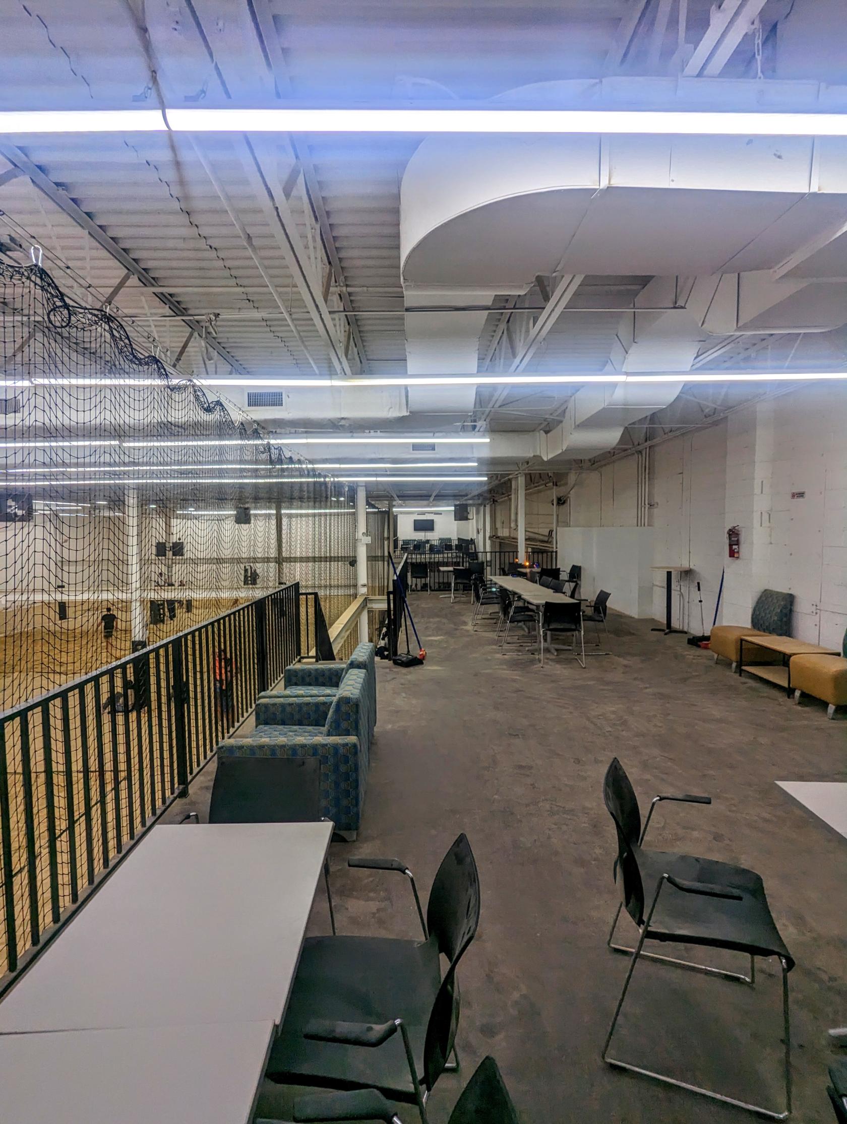 A spacious warehouse with exposed ceiling beams, a seating area with chairs and sofas, and netted sand volleyball courts at Giant warehouse with 3 sand volleyball courts.