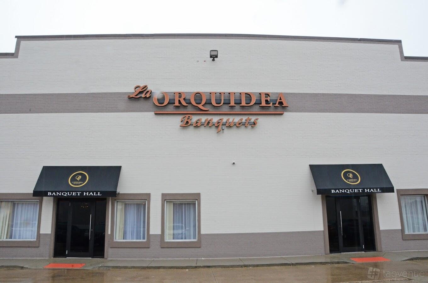 A hall with a white brick exterior, black awnings, and large orange signage at La Orquidea Banquet Hall.
