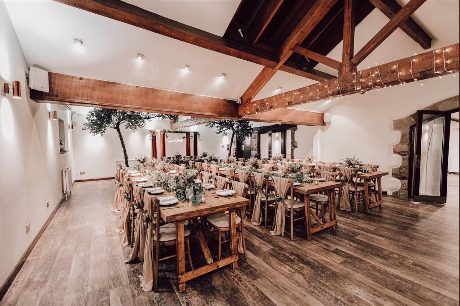 An event space with exposed wooden beams, banquet tables with neutral linens, and greenery at Mercure Tankersley Manor Hotel and Spa.