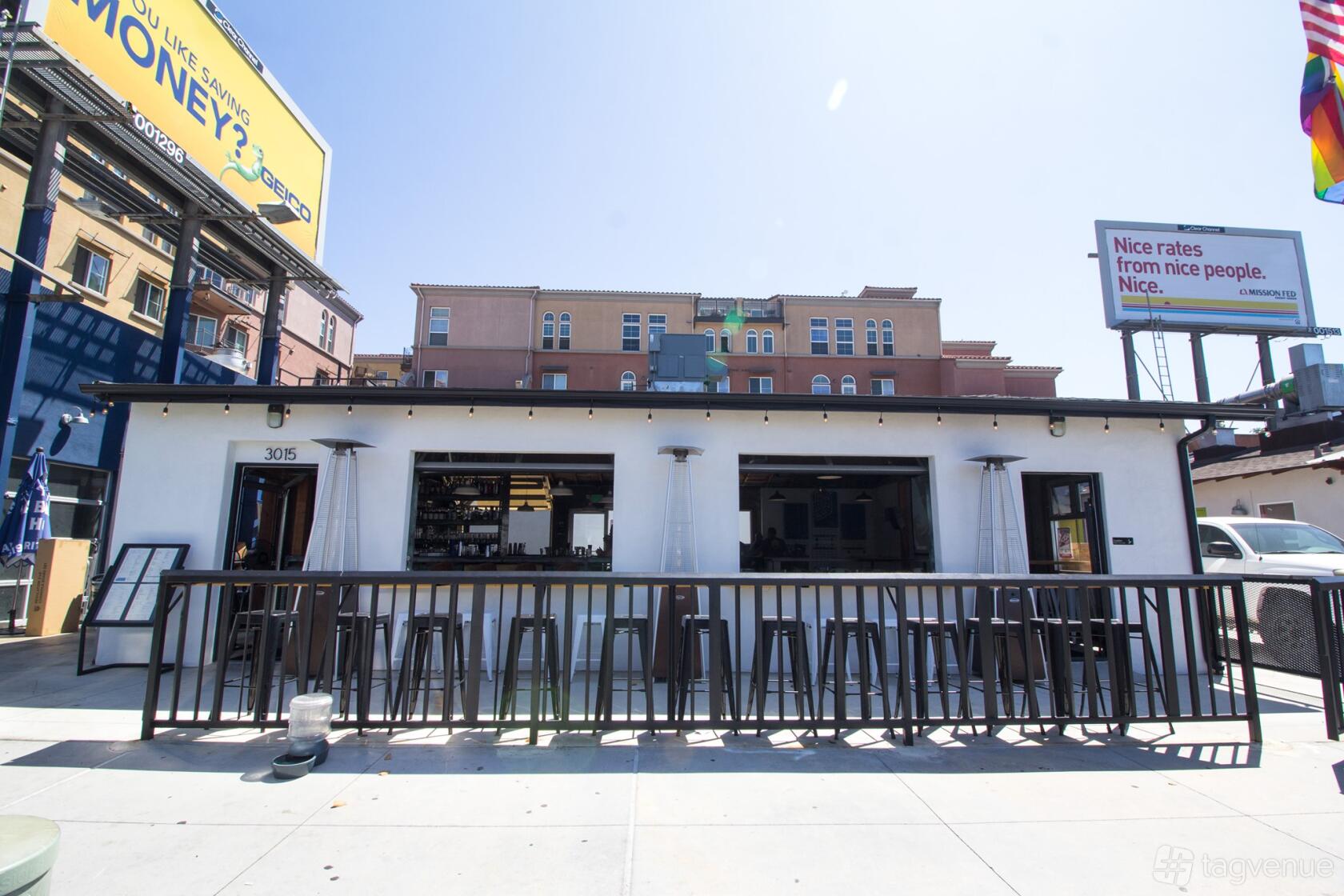 A restaurant with an open-air bar and black metal stools along the sidewalk at 619 Spirits North Park.