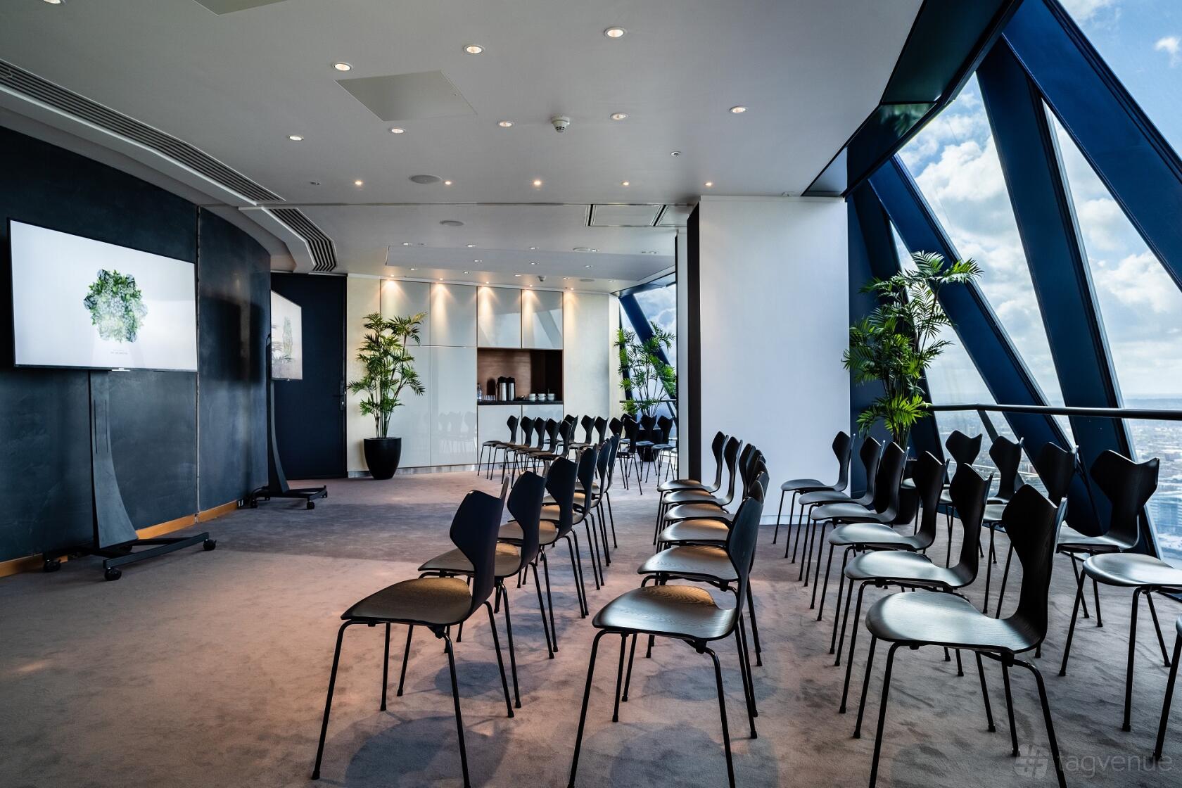 A function room with floor-to-ceiling windows, modern chairs, and potted plants at Searcys at The Gherkin.