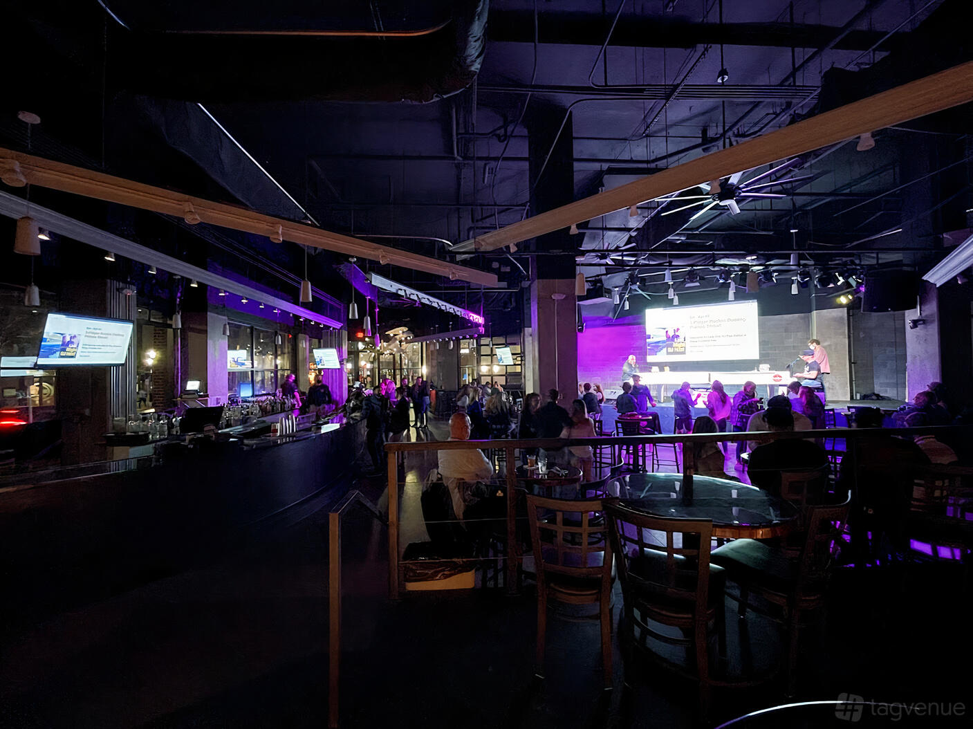 A bar with floor-to-ceiling windows, stage lighting, and high-top tables at Park Bench Battery.