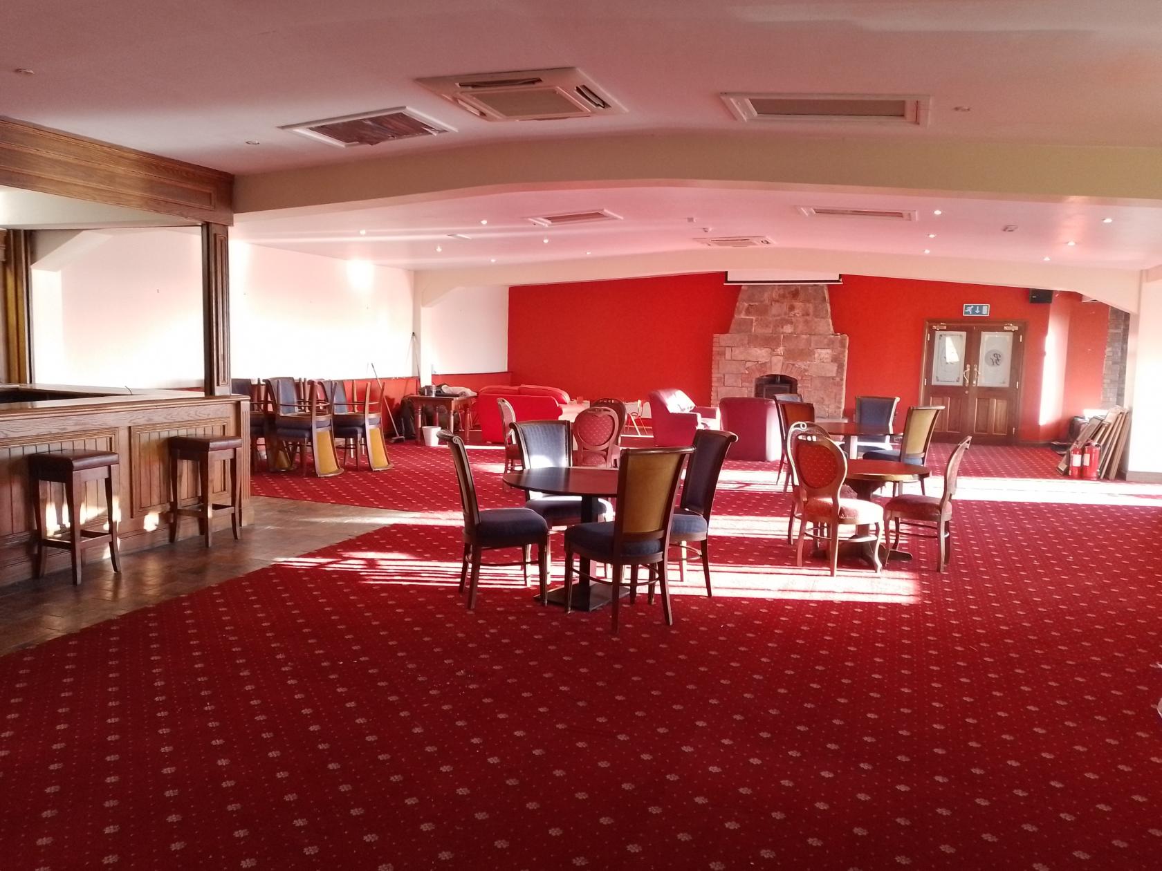 An event venue with red carpet flooring, scattered tables and chairs, and a stone fireplace at Puddenhill.