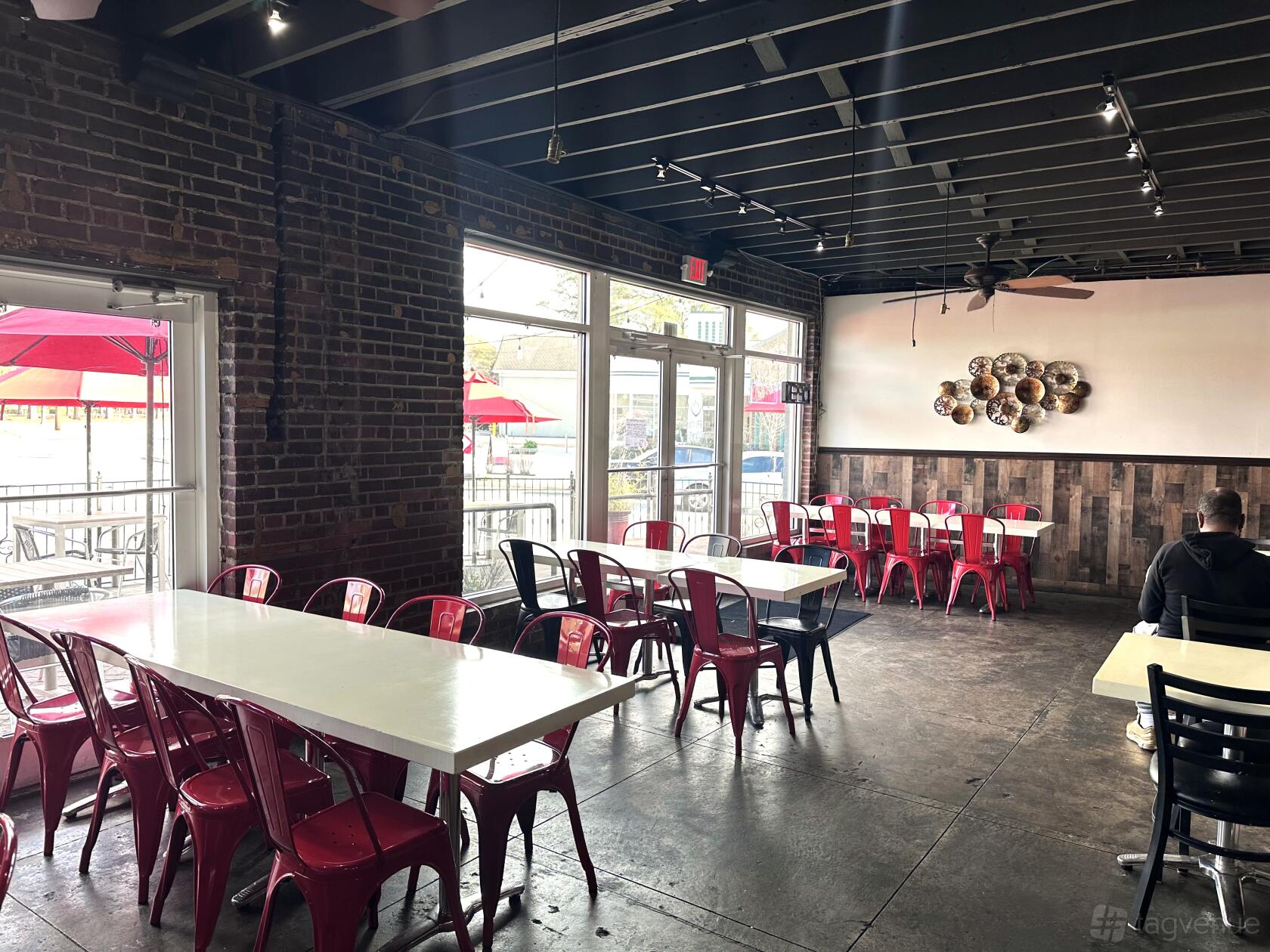 An event space in a restaurant with exposed brick walls, red metal chairs, and large windows at Dua Hapeville.