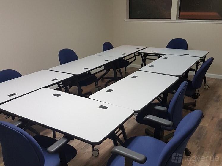 A meeting room with modular white tables in a U-shape and blue office chairs at Action Spot.