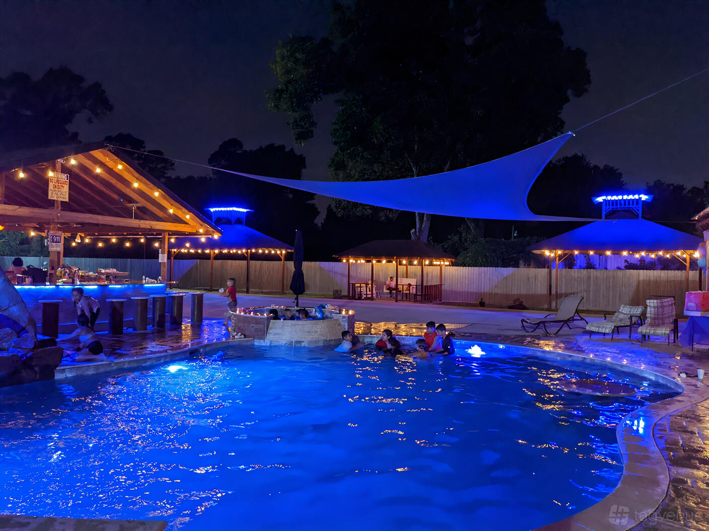 An outdoor event venue with a pool, swim-up bar, string lights, and shaded seating areas at Martinez Eventos.