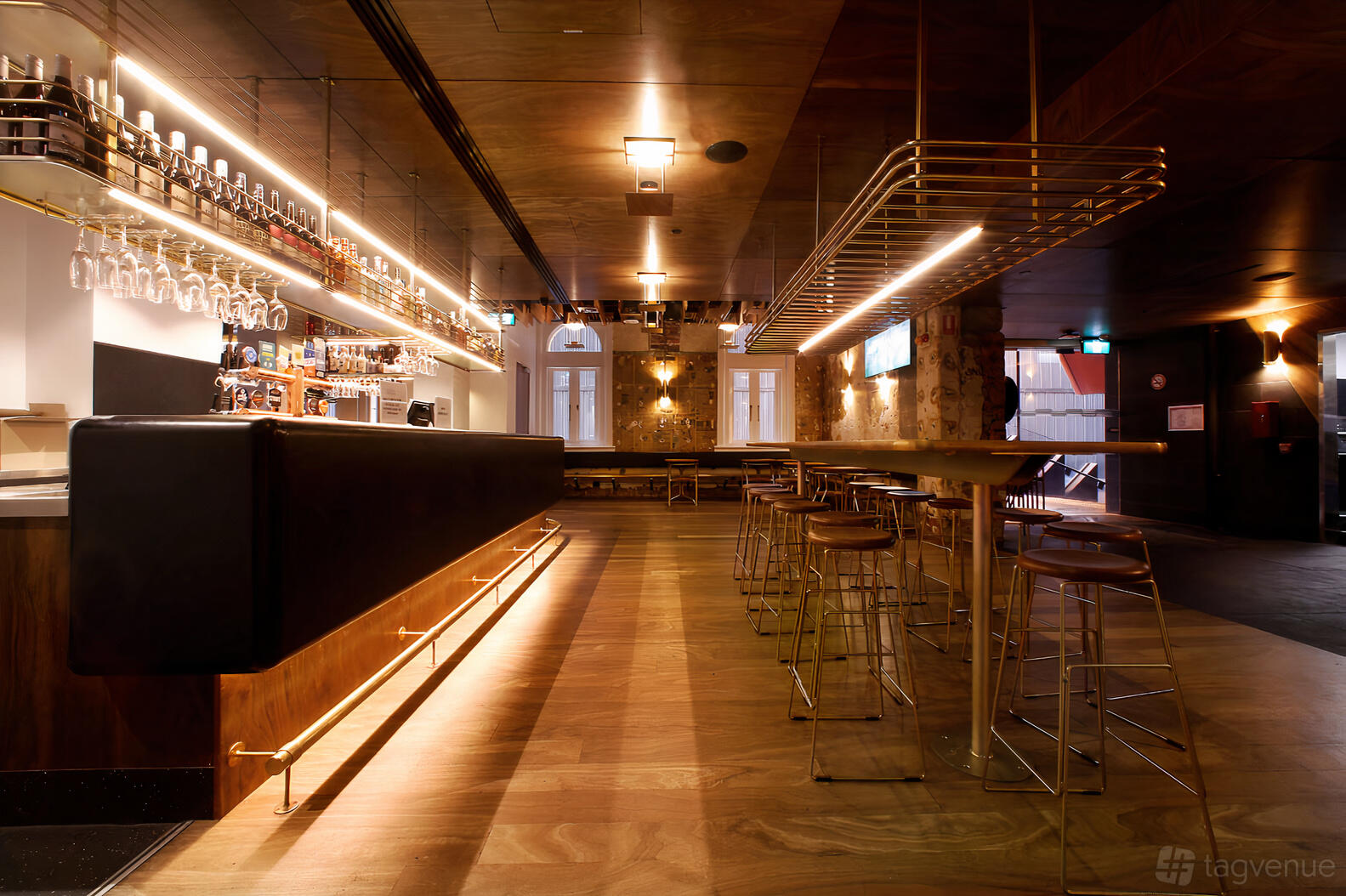 An event space in a pub with wooden floors, high tables and stools, exposed stone walls, and a long bar at The Oxford Scholar.