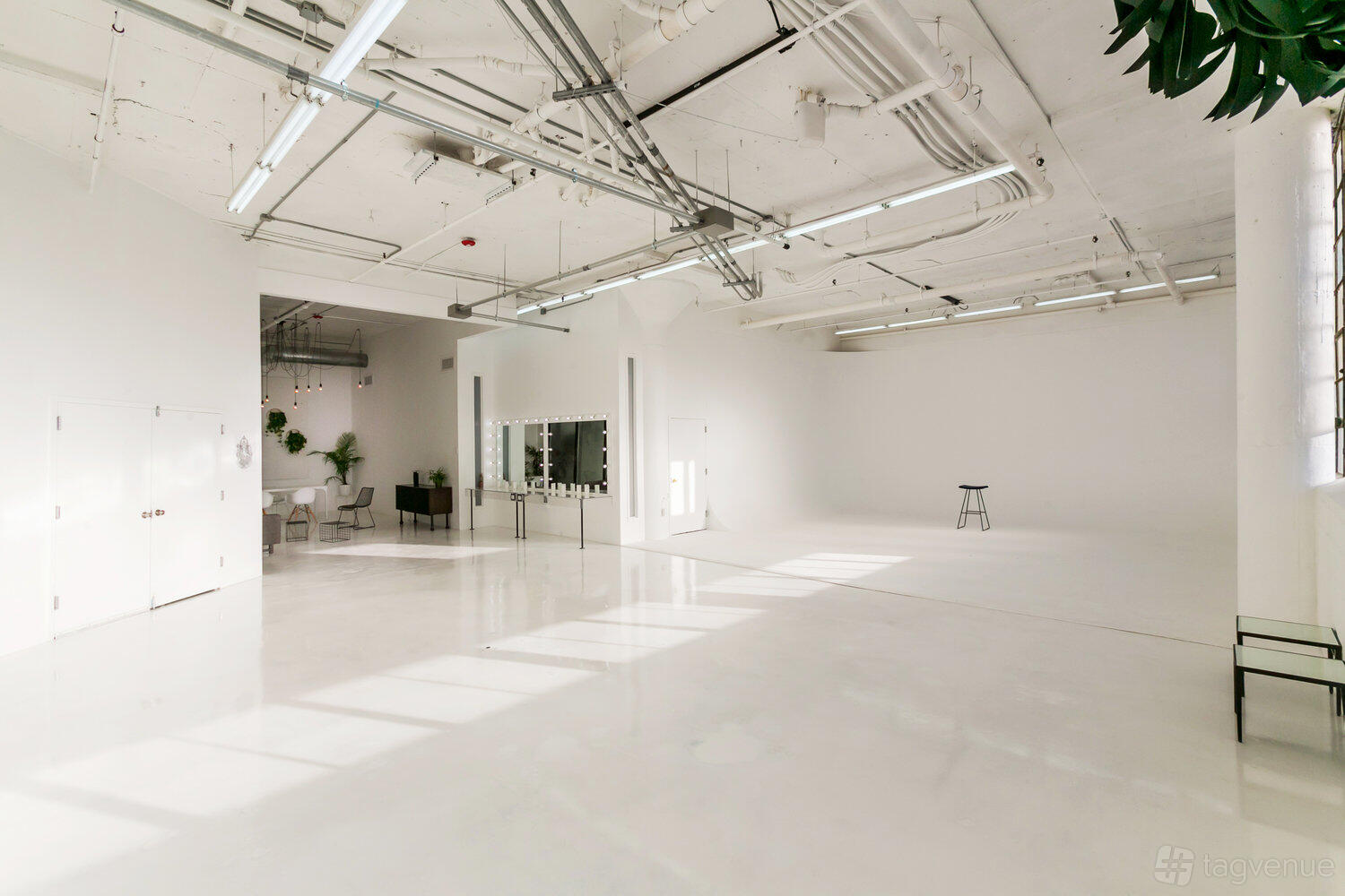 A photo studio with white walls, high ceilings, natural light, a single stool, and a large mirror at 7 Line Studio.
