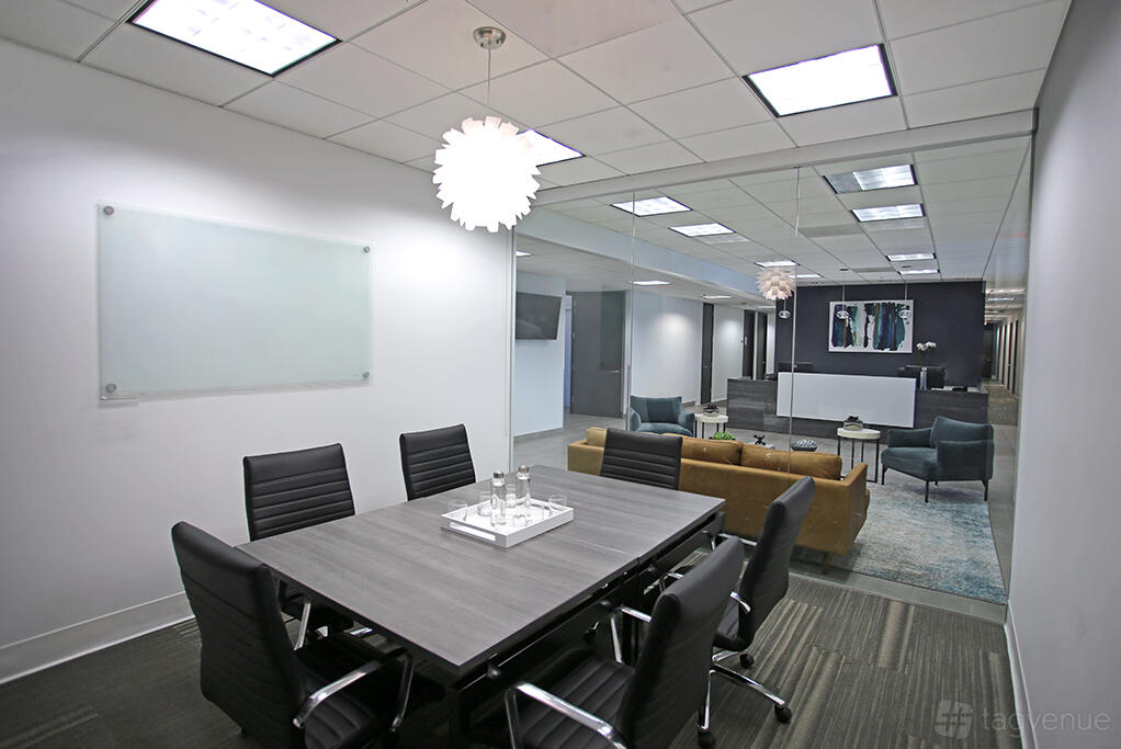 A meeting room with a rectangular table, six black chairs, and a glass board at Premier Workspaces - 444 W Ocean.