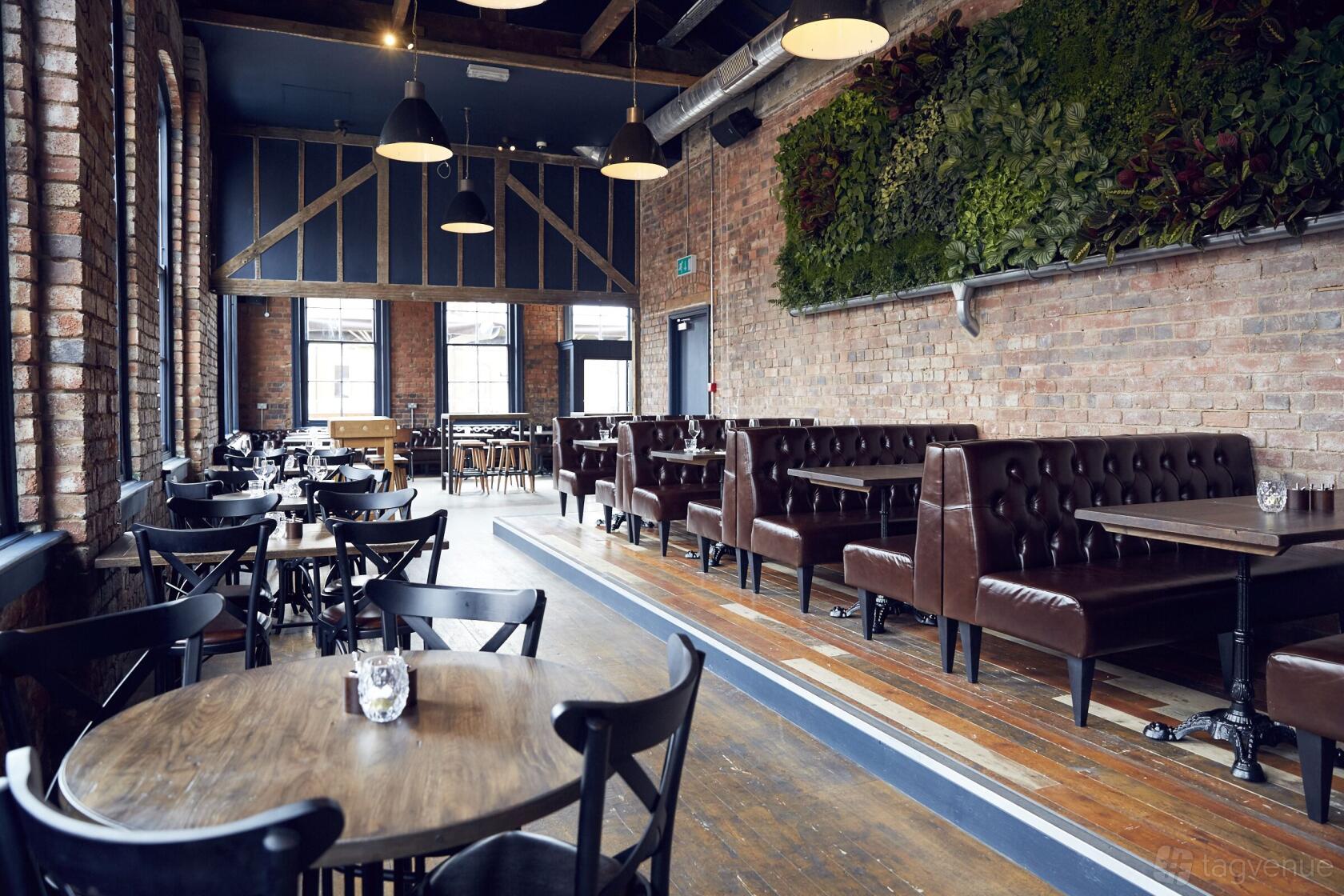 An event space in a pub with exposed brick walls, brown leather booths, and a living plant wall at The Button Factory.