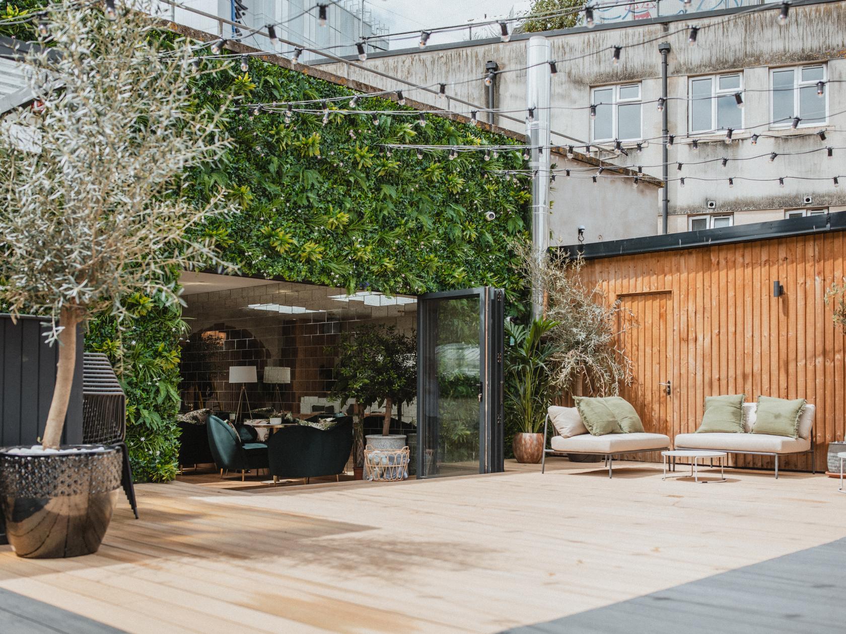 A rooftop event space with wooden decking, greenery wall, string lights, and outdoor lounge seating at Armada House.