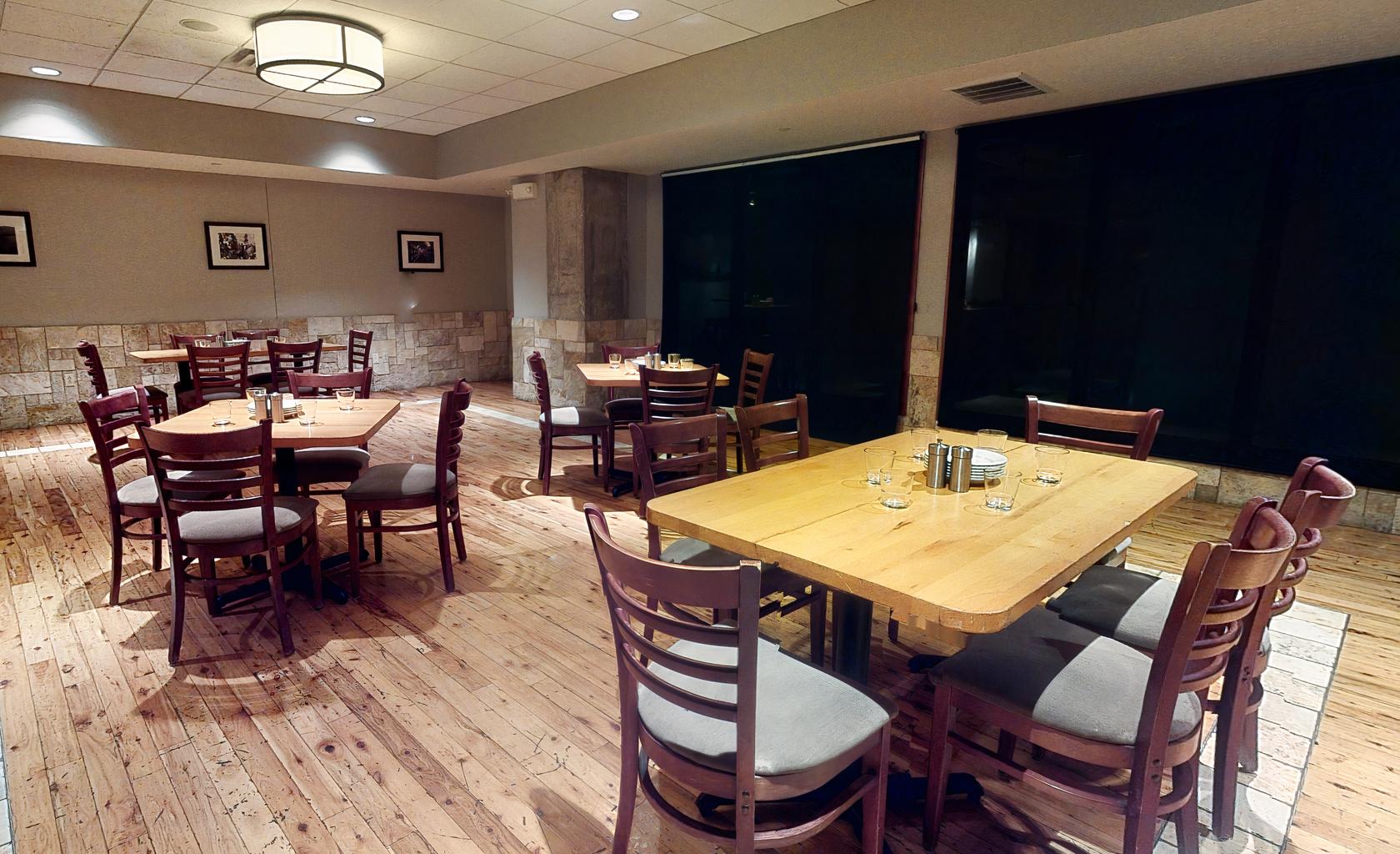 A restaurant dining room with wooden floors, square wooden tables, and cushioned chairs at Pinstripes - Georgetown DC.