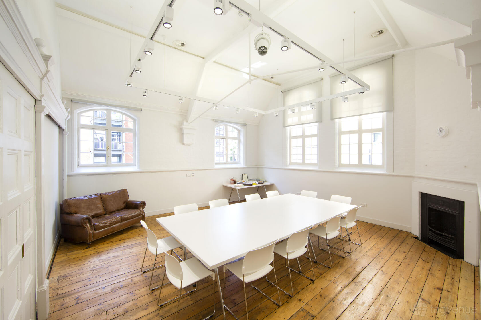 A meeting room with a large white table, white chairs, exposed wood floors, and tall windows at The Goldsmiths' Centre.
