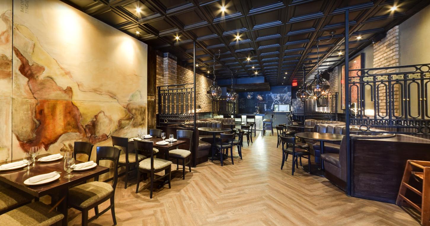 A restaurant with herringbone wood floors, dark wood tables, and a large abstract mural at Sher-E-Punjab.