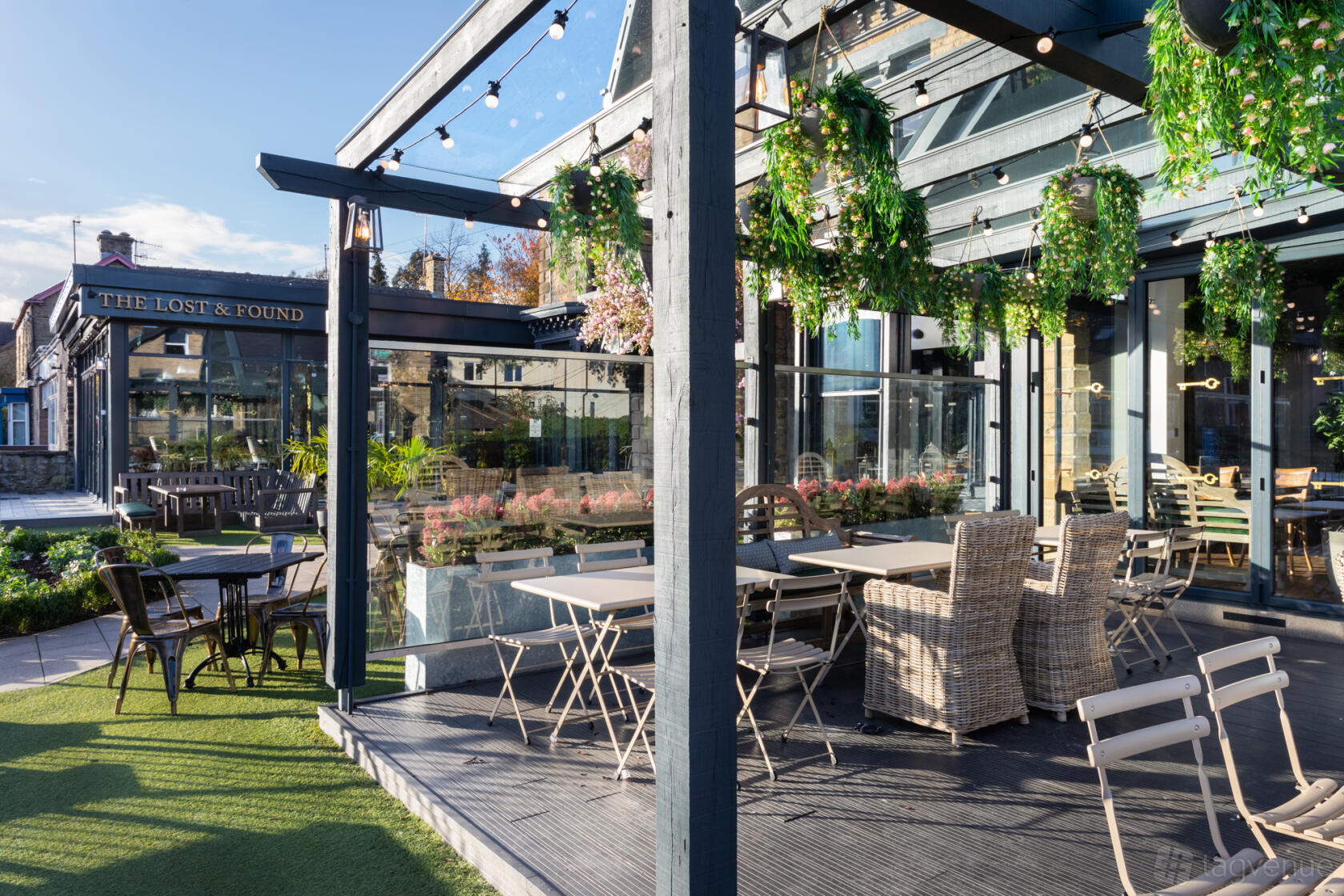 A terrace bar with glass walls, hanging greenery, wicker seating, and bistro tables at The Lost and Found Sheffield.
