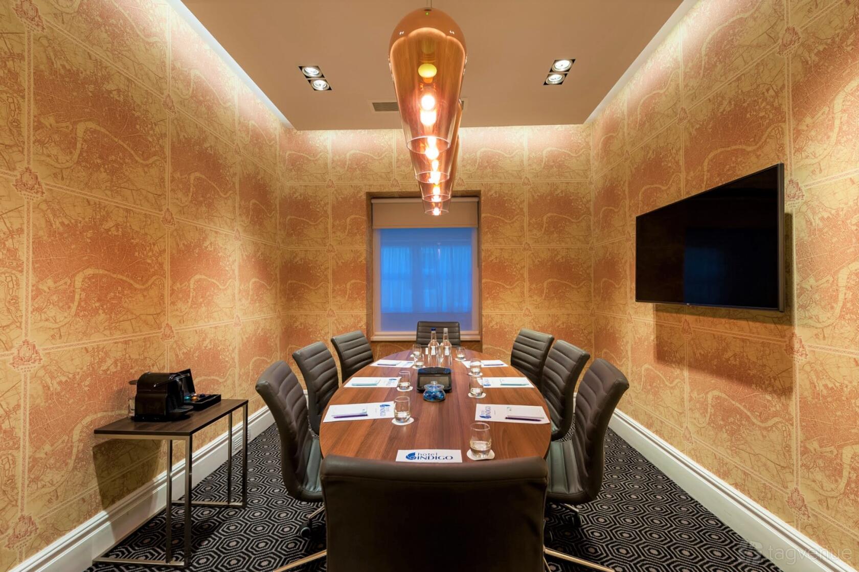 A meeting room with patterned wallpaper, a long table, leather chairs, and a pendant light at Mercure London Hyde Park.
