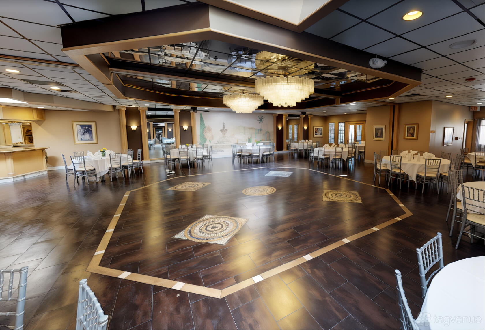 An event space in a restaurant with geometric wood floors, chandeliers, and round tables at Angelo's Ristorante.