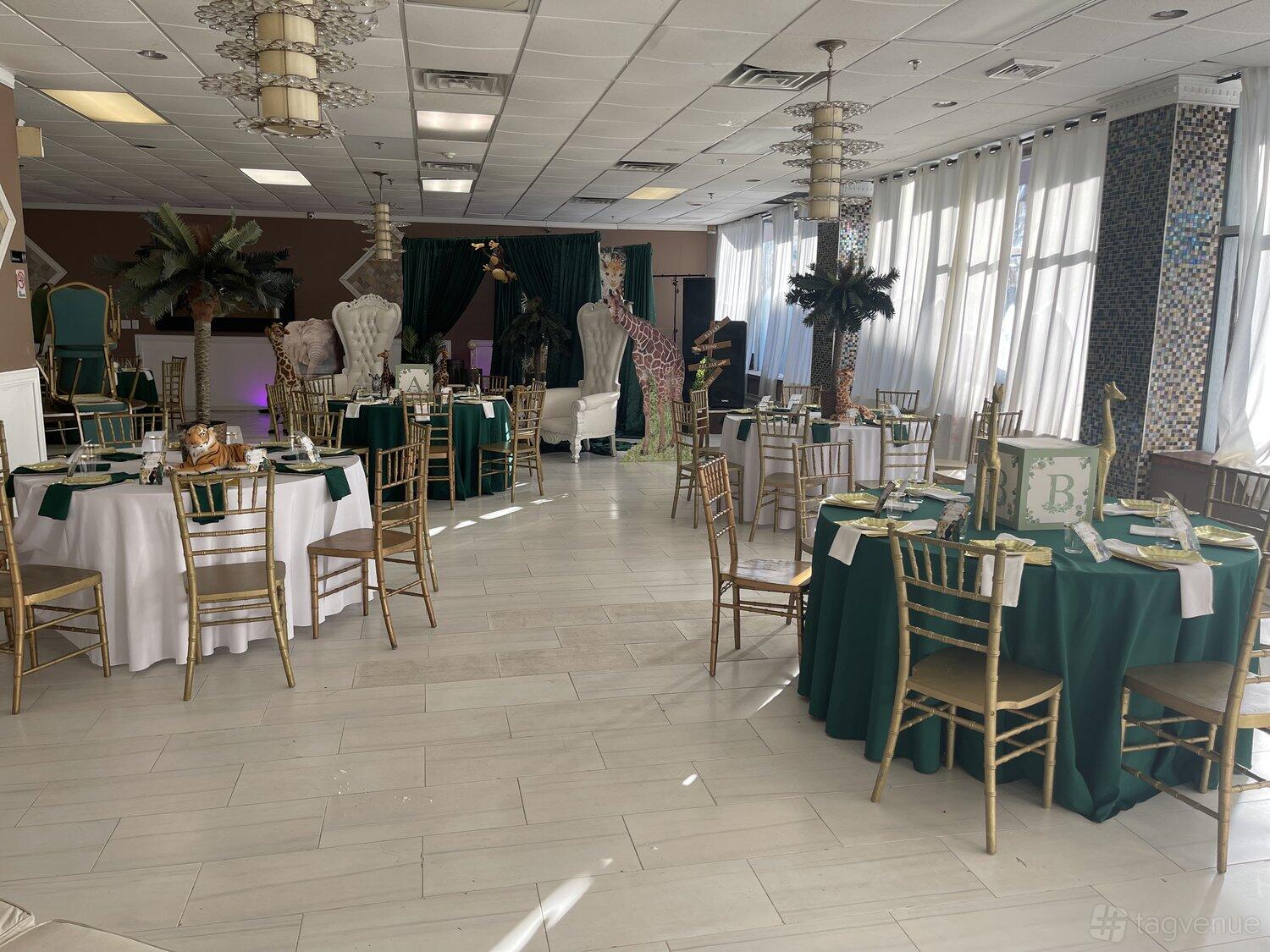 A banquet hall with round tables draped in white and green linens, gold chairs, and tall decorative palm trees at TLO Event Complex.
