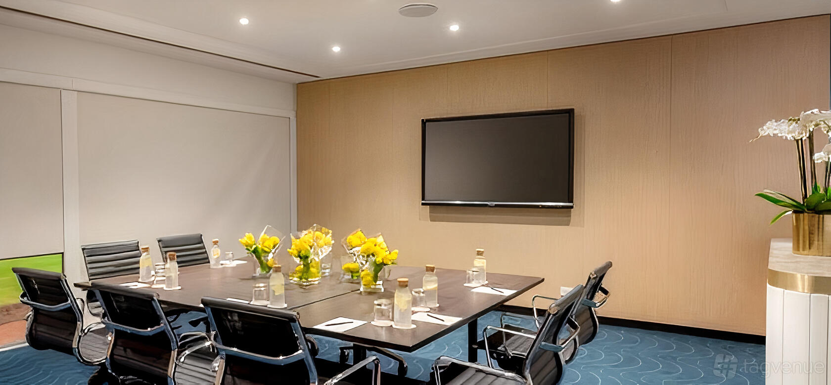 A hotel meeting room with a large conference table, leather chairs, a wall-mounted screen, and floral centerpieces at Novotel Sydney Darling Square.