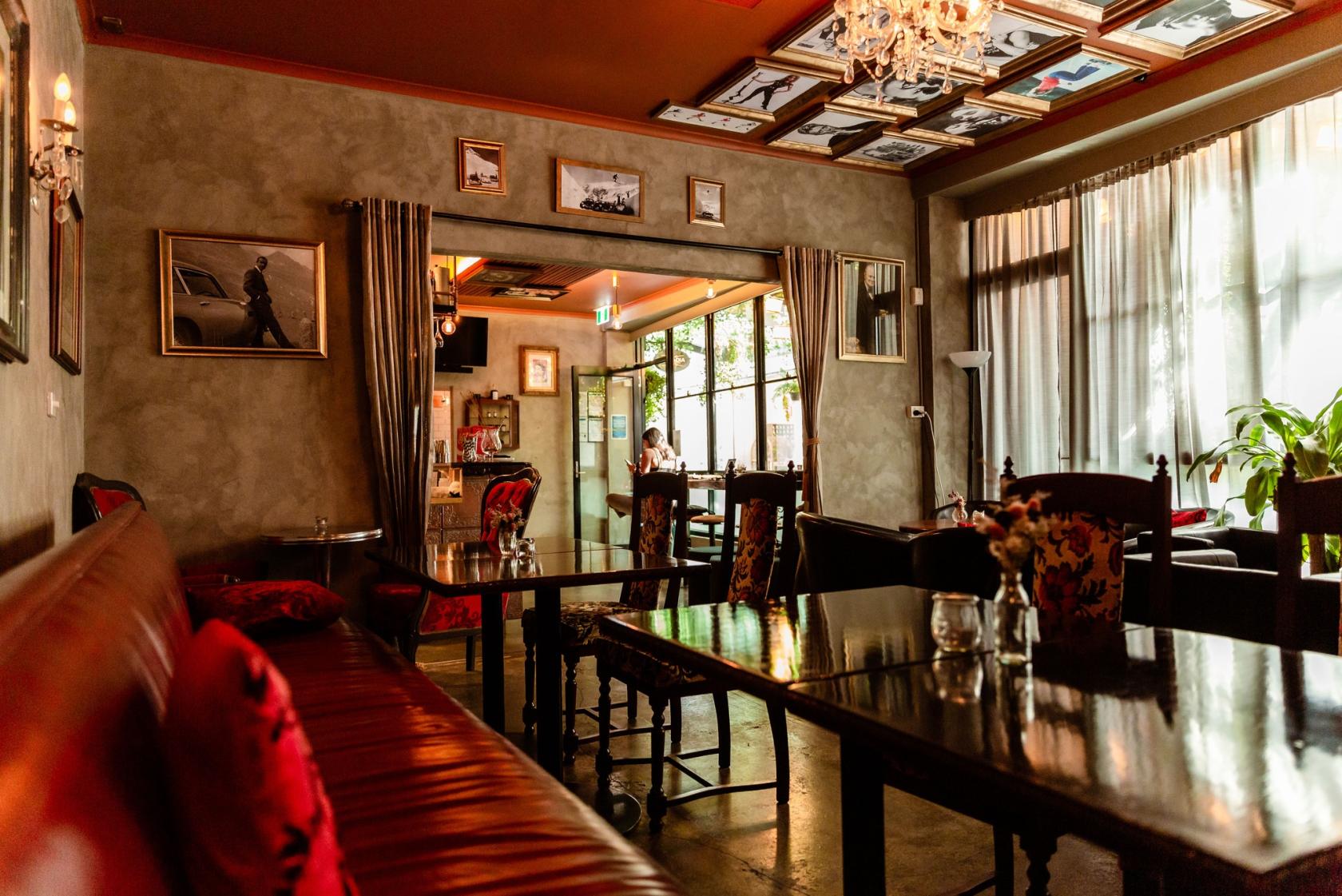 A bar with leather banquette seating, framed photos, chandeliers, and floor-to-ceiling windows at Arcadia Whisky Lounge.