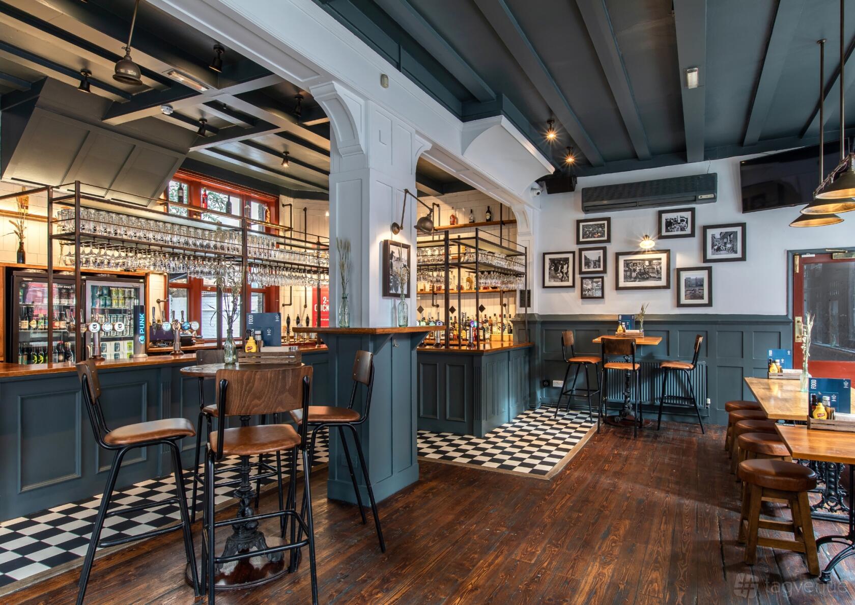 A pub with a wooden floor, checkered tile accents, framed wall photos, and a central wood bar at Duke of Hammersmith.