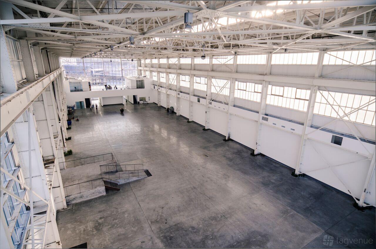 A spacious warehouse with soaring ceilings, exposed steel beams, and large industrial windows at Duggal Greenhouse.