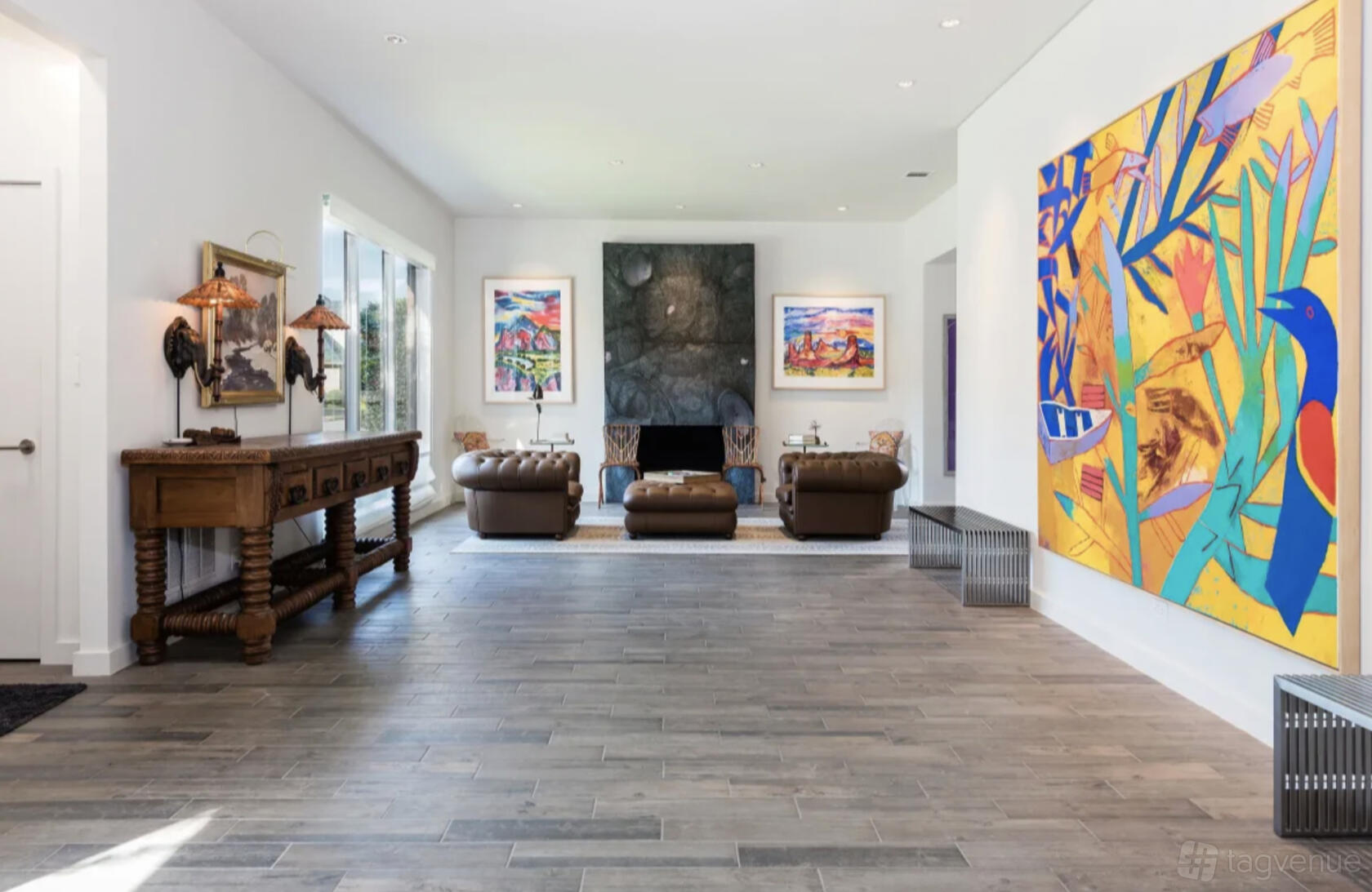 A house with large colorful artwork, a wooden console table, and leather armchairs around a fireplace at Contemporary & Spacious Urban Home.