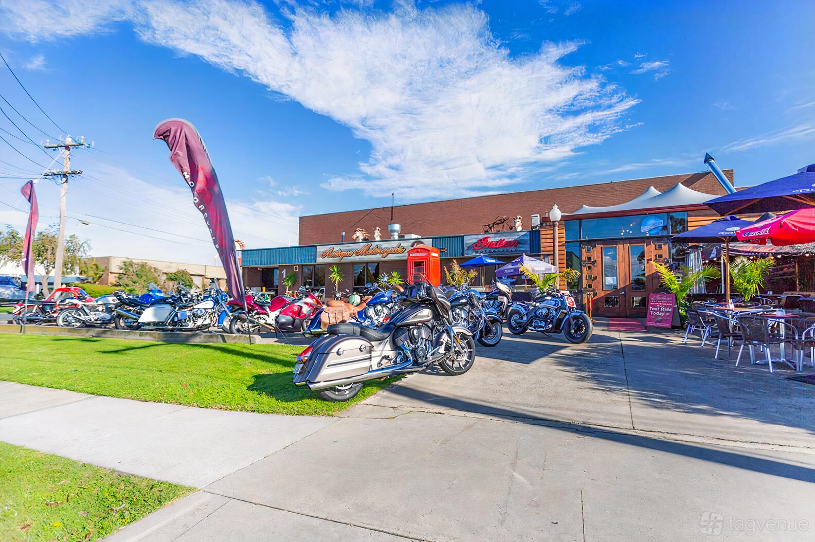 A pub with motorcycles parked along the sidewalk, outdoor seating, and red umbrellas at Naked Racer Bar & Cafe.
