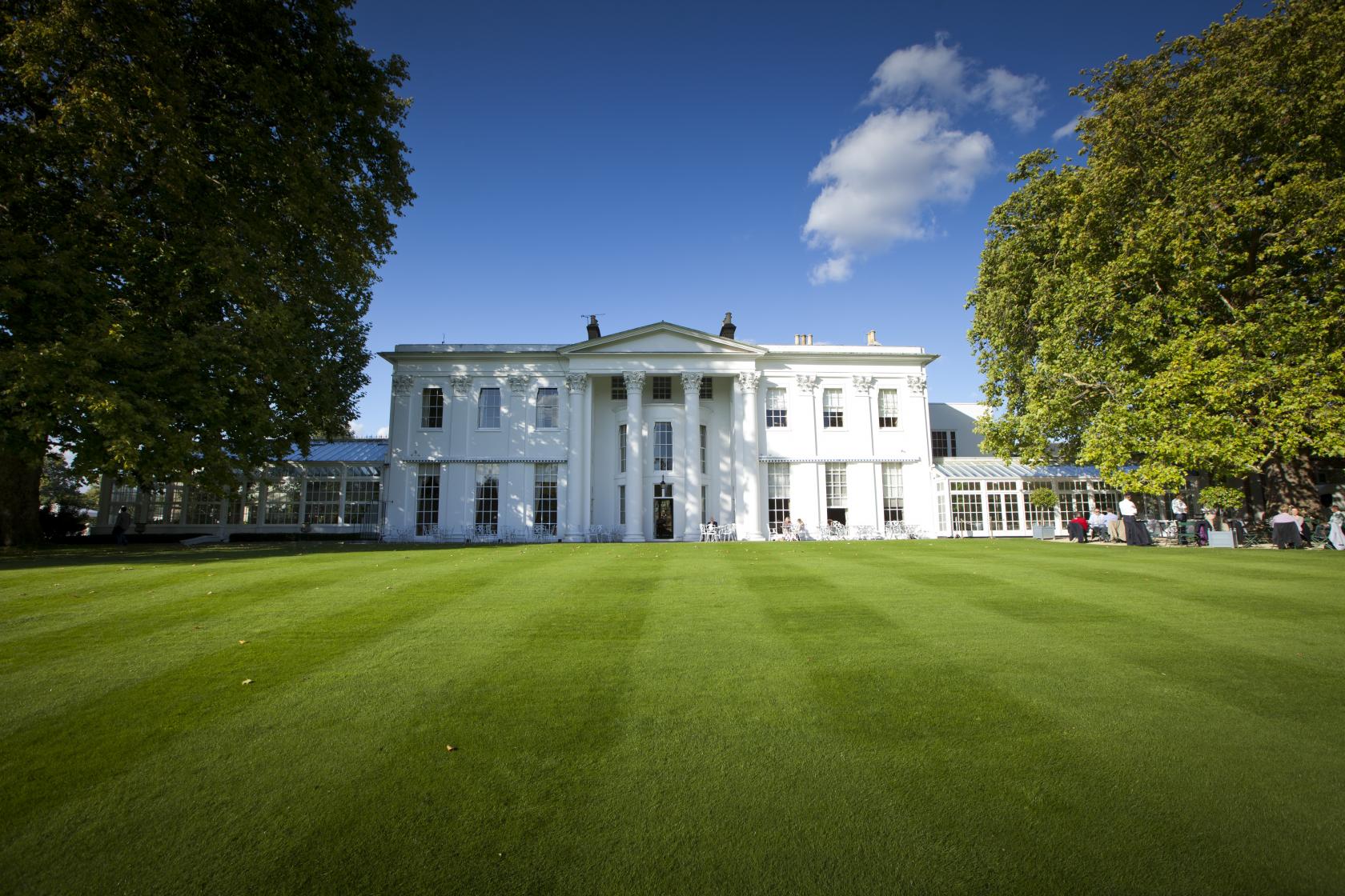 A versatile event space with a white neoclassical façade and expansive manicured lawn at The Hurlingham Club.