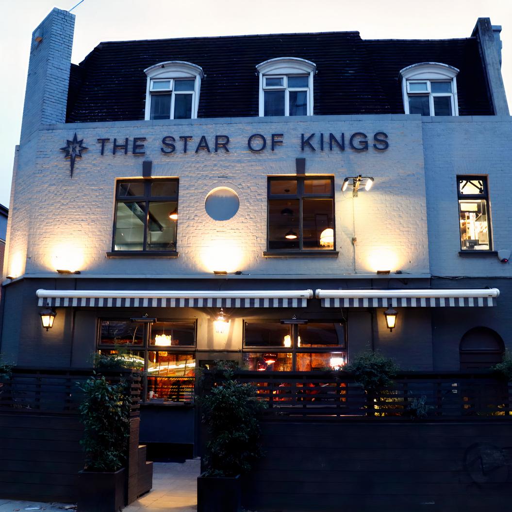 The exterior of a pub with illuminated signage, striped awning, and large front windows at Star of Kings.