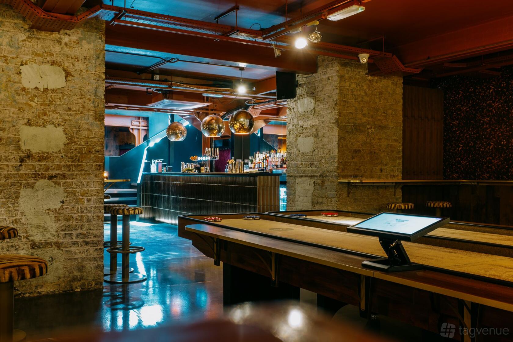 An event venue with exposed brick columns, shuffleboard tables, and a bar with globe pendant lights at Shuffle Club.