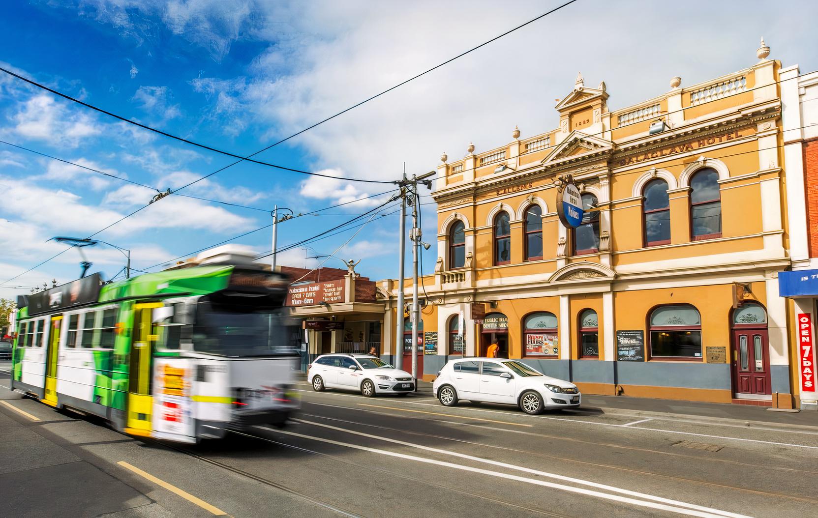 A pub with a historic yellow facade, arched windows, and streetcar passing outside at Balaclava Hotel.