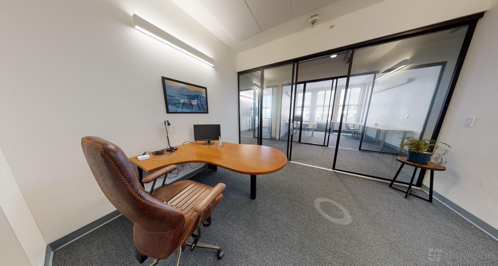An office space with a curved wooden desk, leather chair, glass walls, and natural light at Dynamico Space.