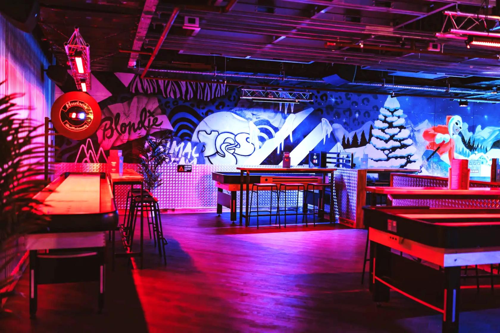A bowling alley lounge with neon lighting, wall murals, and high-top tables at Roxy Lanes Edinburgh Rose Street.