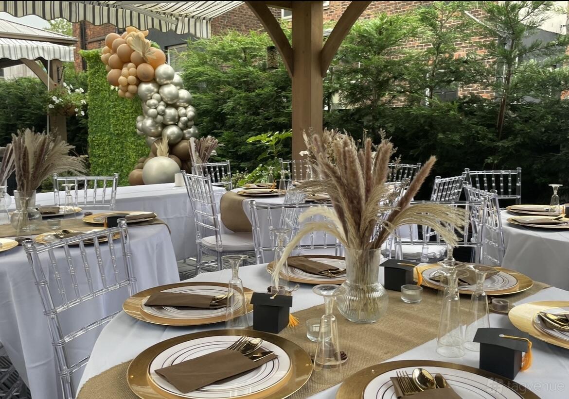 An outdoor terrace with round tables dressed in white linens, gold accents, and balloon decorations at The Urban Courtyard Manchester.