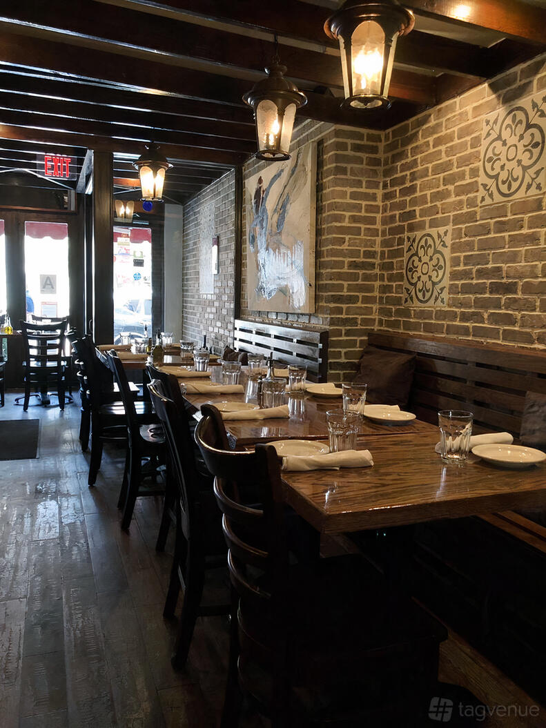 A restaurant dining area with exposed brick walls, wood tables set with white plates and glasses at Balade.