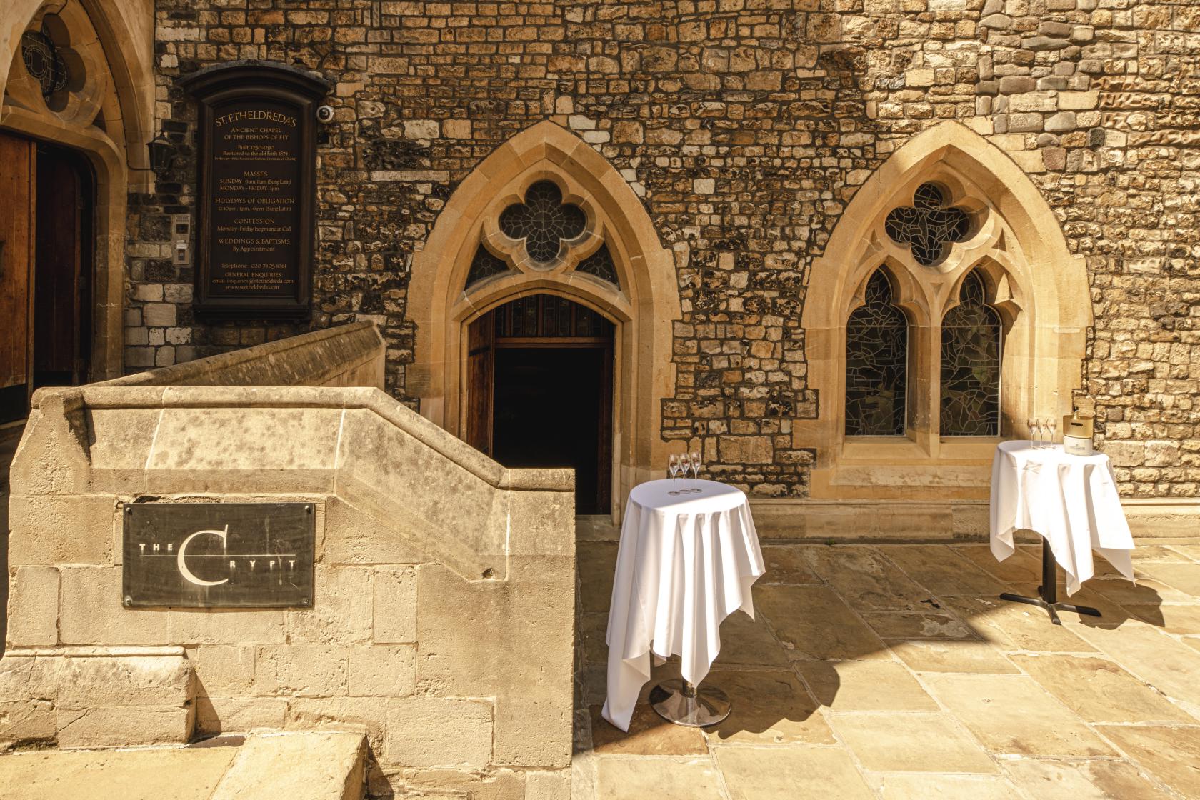A historic building with arched stone windows, gothic detailing, and cocktail tables with linens at The Crypt.