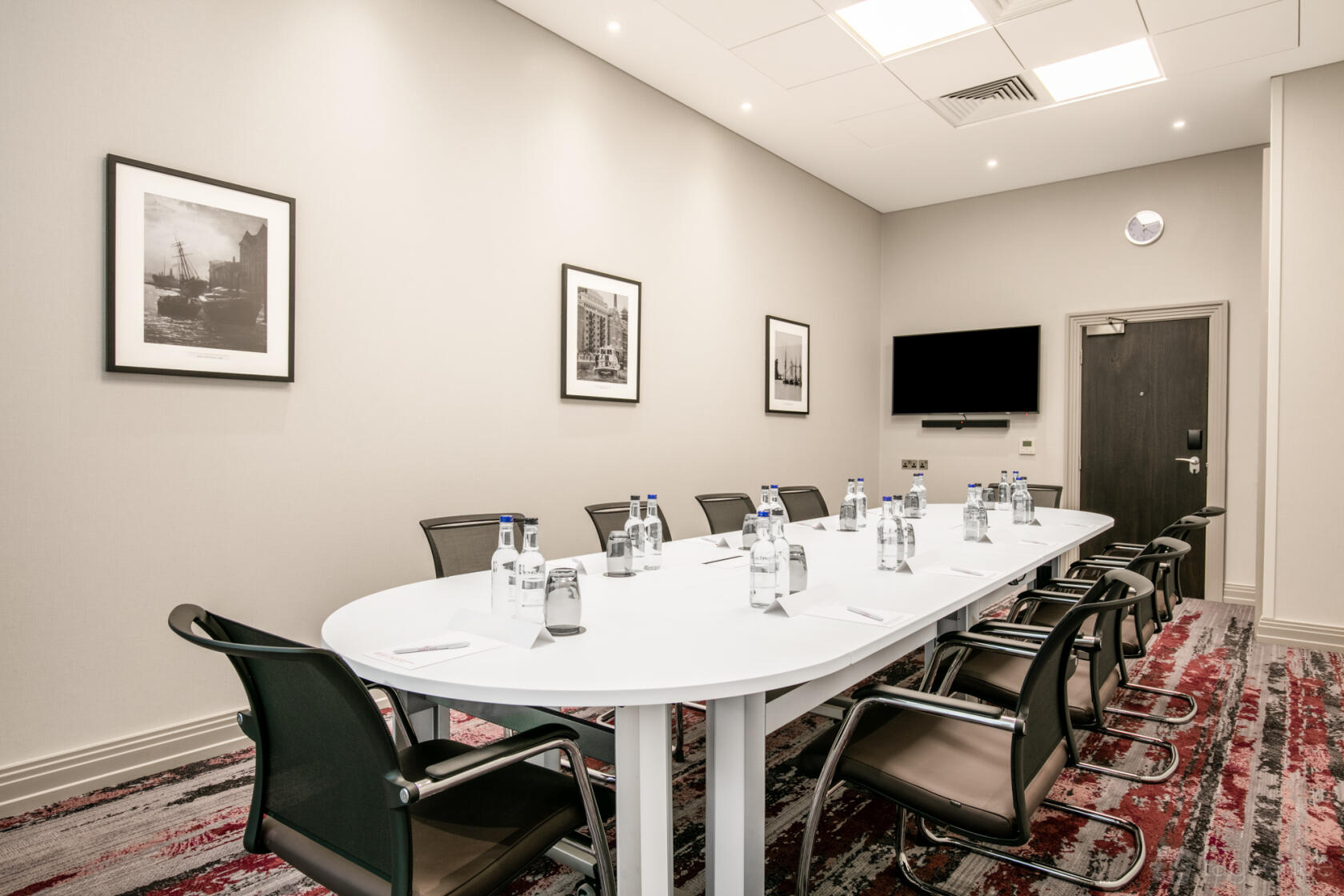 A meeting suite with an oval table, black chairs, wall art, and a mounted TV at Crowne Plaza London Docklands.