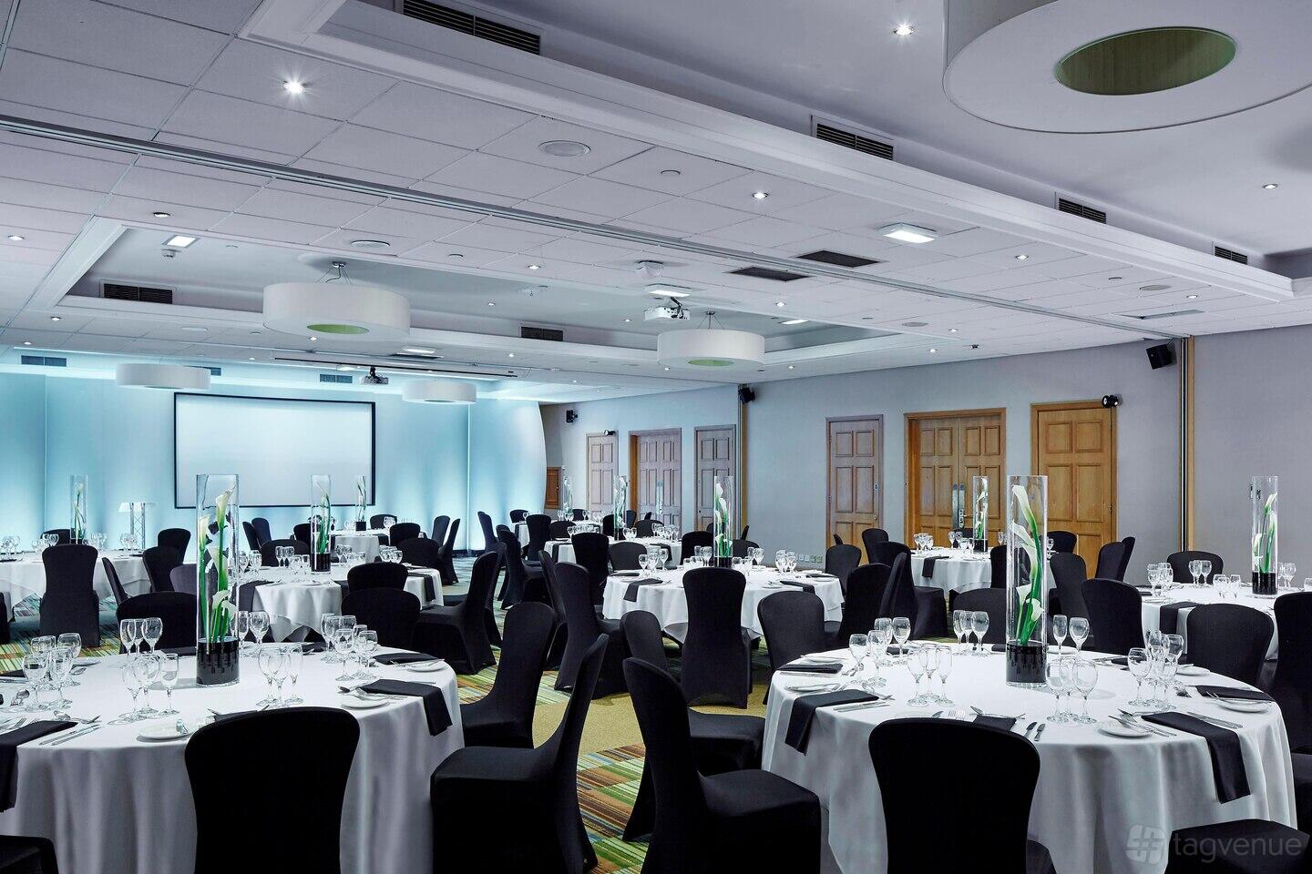 An event space with round tables dressed in white linens, black chairs, and a projector screen at Marriott Victoria & Albert Hotel.