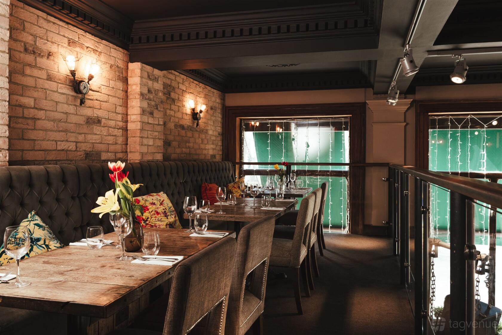 An event space in a restaurant with tufted banquette seating, exposed brick walls, and set dining tables at Balfour St Bart's