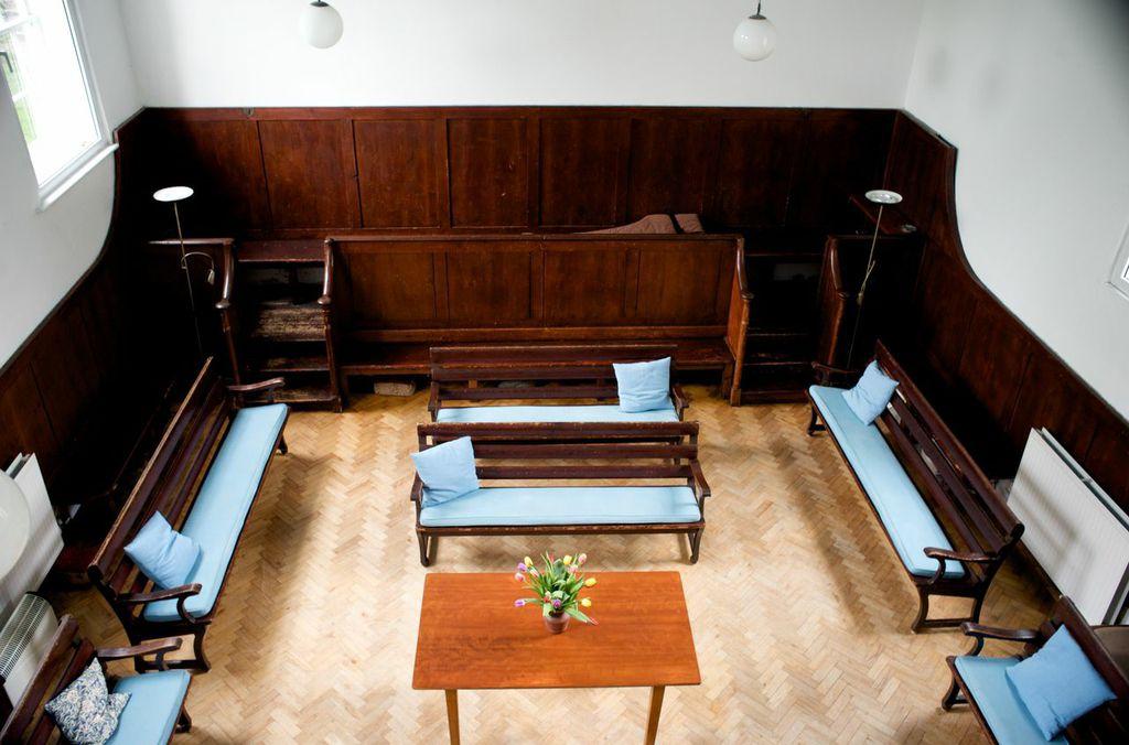 A church with wood-paneled walls, simple wooden benches with blue cushions, and a wooden table at Brentford & Isleworth Quaker Meeting House.