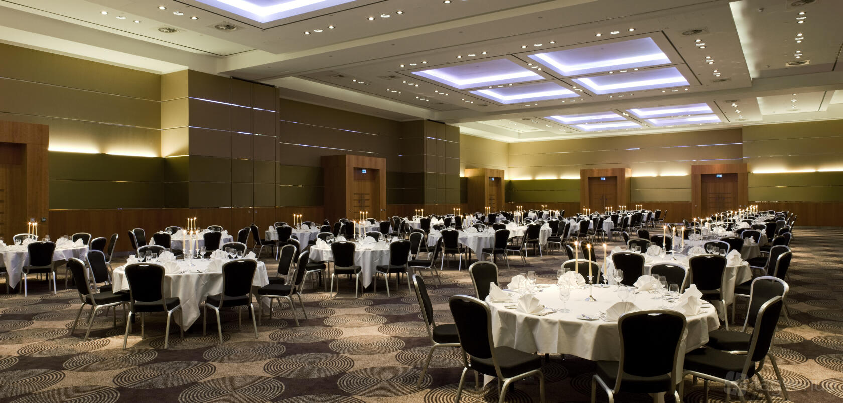 An event space with round tables draped in white linens, black chairs, and soft ceiling lights at Sofitel London Heathrow.