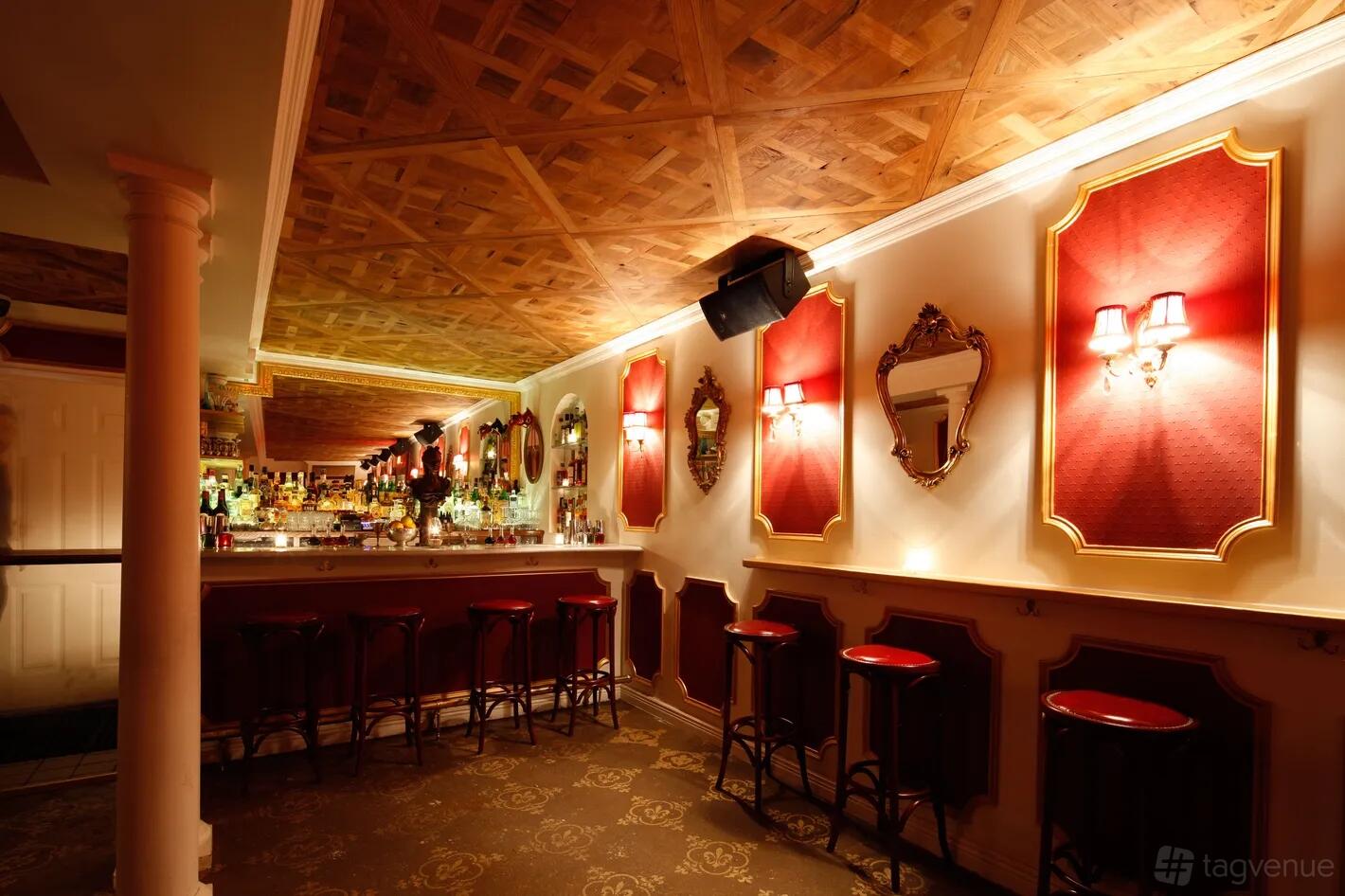 A restaurant with red velvet stools, ornate mirrors, wall sconces, and a wooden ceiling at Chez Moi.