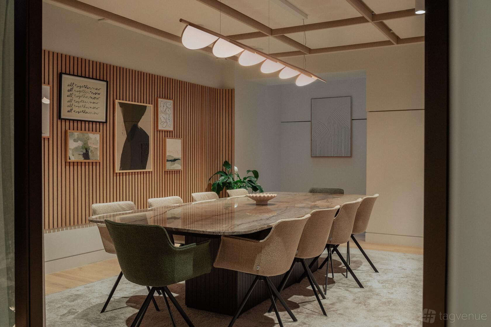 A meeting room with a marble conference table, cushioned chairs, and wood slat walls with art at Uncommon Holborn.
