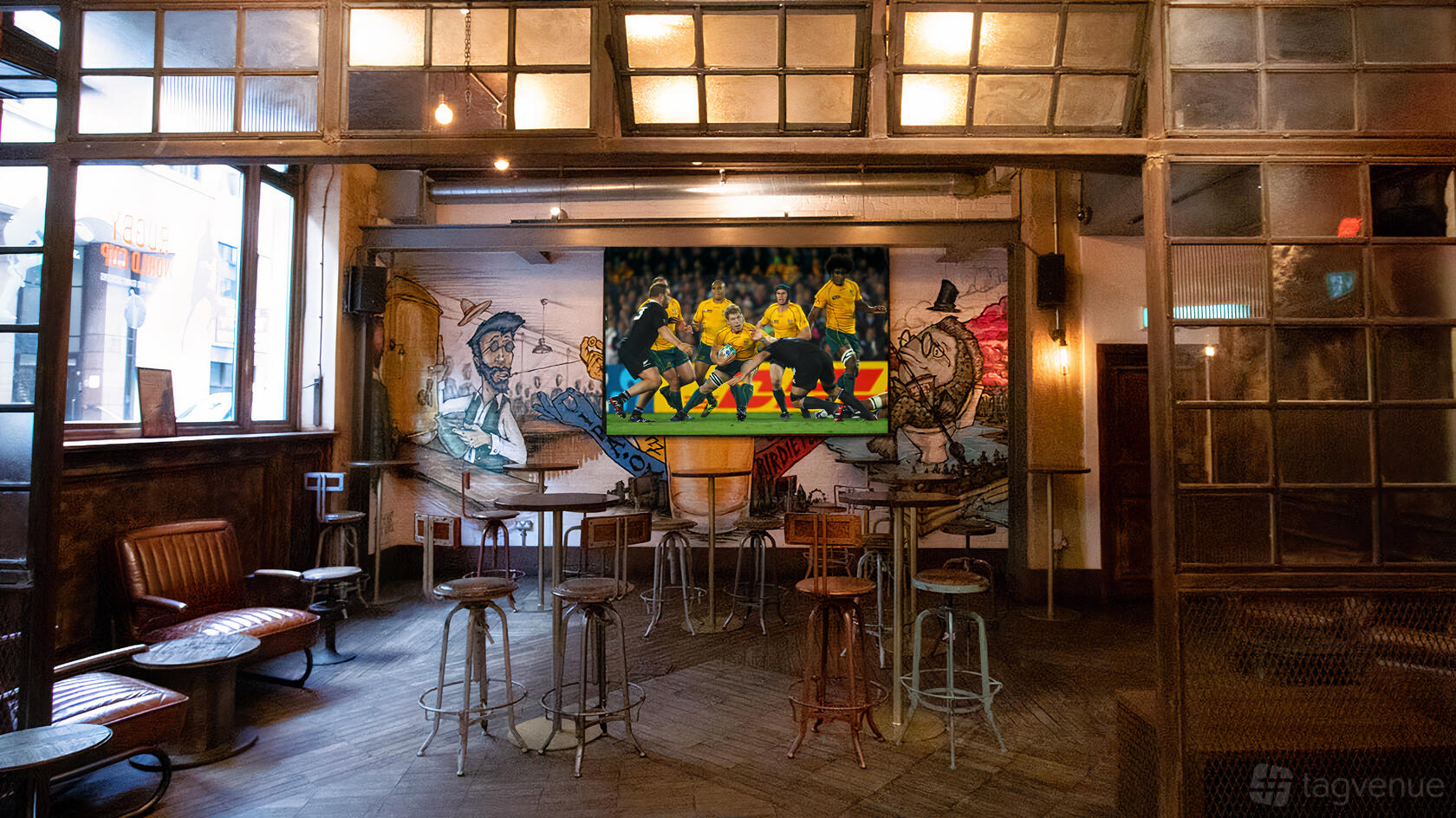 A pub bar with high tables, bar stools, a mural wall, and a large screen displaying a football match at Long Arm Brewery & Tap Room.